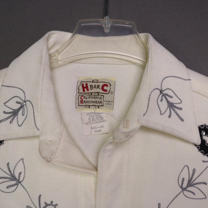 This vintage 1970s H Bar C California Ranchwear "Taos" cream polyester fabric, white fringe detailing, and black and gray floral embroidery with pearl snap