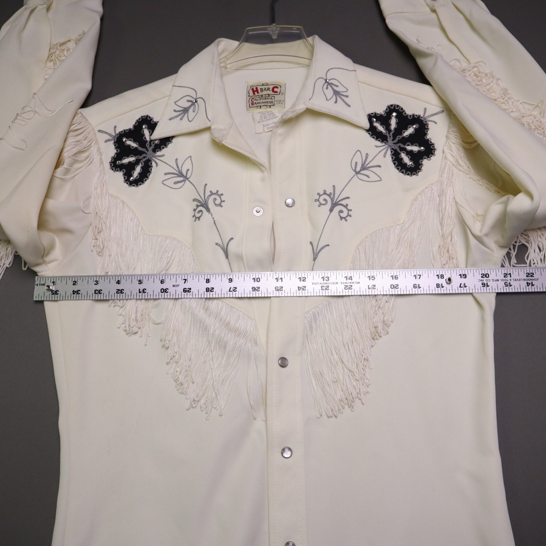 This vintage 1970s H Bar C California Ranchwear "Taos" cream polyester fabric, white fringe detailing, and black and gray floral embroidery with pearl snap