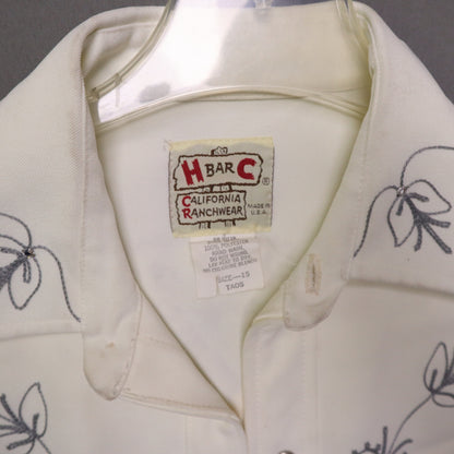 This vintage 1970s H Bar C California Ranchwear "Taos" cream polyester fabric, white fringe detailing, and black and gray floral embroidery with pearl snap